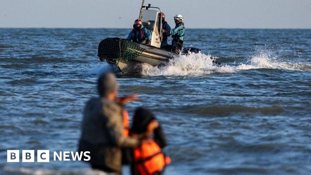 A French Navy boat sails past migrants trying to board a boat in an attempt to cross the English Channel
