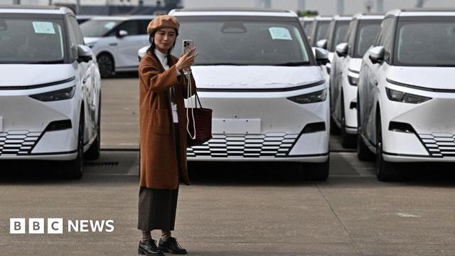 A woman takes a selfie in front X9 electric vehicles by Chinese EV manufacturer XPeng, are loaded on ship of the NYK line during a ceremony in the Port of Guangzhou, China's southern Guangdong province, on 22 February, 2025.