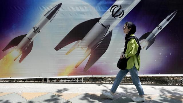 Une femme marche devant une illustration représentant des missiles iraniens.
