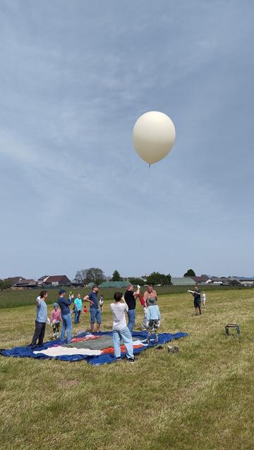 A group of people launching a weather balloon into the blue sky on a green field