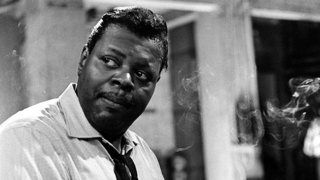 Oscar Peterson, les mains sur le clavier d'un piano, regarde au loin.
