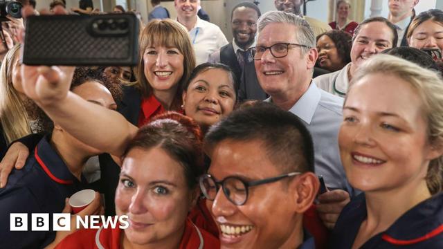 Close up Sir Keir Starmer and Rachel Reeves posing for a selfie taken by an NHS staff member. They are smiling and surrounded by a group of NHS staff all smiling at the camera