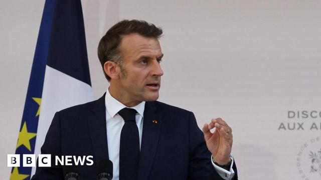 France's President Emmanuel Macron delivers a speech to army leaders. He is standing in front of a French and EU flag and is gesturing with his left hand as he speaks.