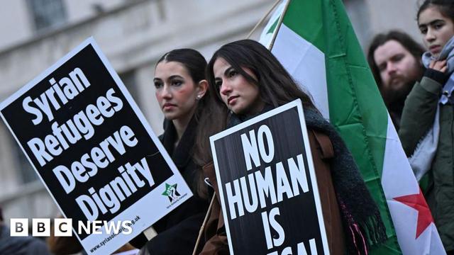 Two female protesters hold Syrian flags and placards reading: "Syrian refugees deserve dignity" and "no human is illegal".