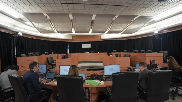 Cinq personnes installées devant leurs postes de travail dans la salle d'une commission d'enquête.