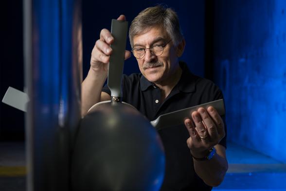 A man is adjusting a propeller blade attached to a test model, with a blue-lit background.