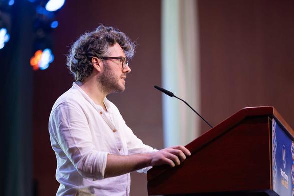 Man with glasses speaking at a podium with a microphone in a conference setting. Man with glasses speaking at a podium with a microphone in a conference setting.