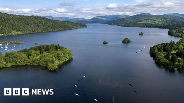 A drone view of Lake Windermere. Boats can be seen o the lake and trees and fields line the lake shoreline.